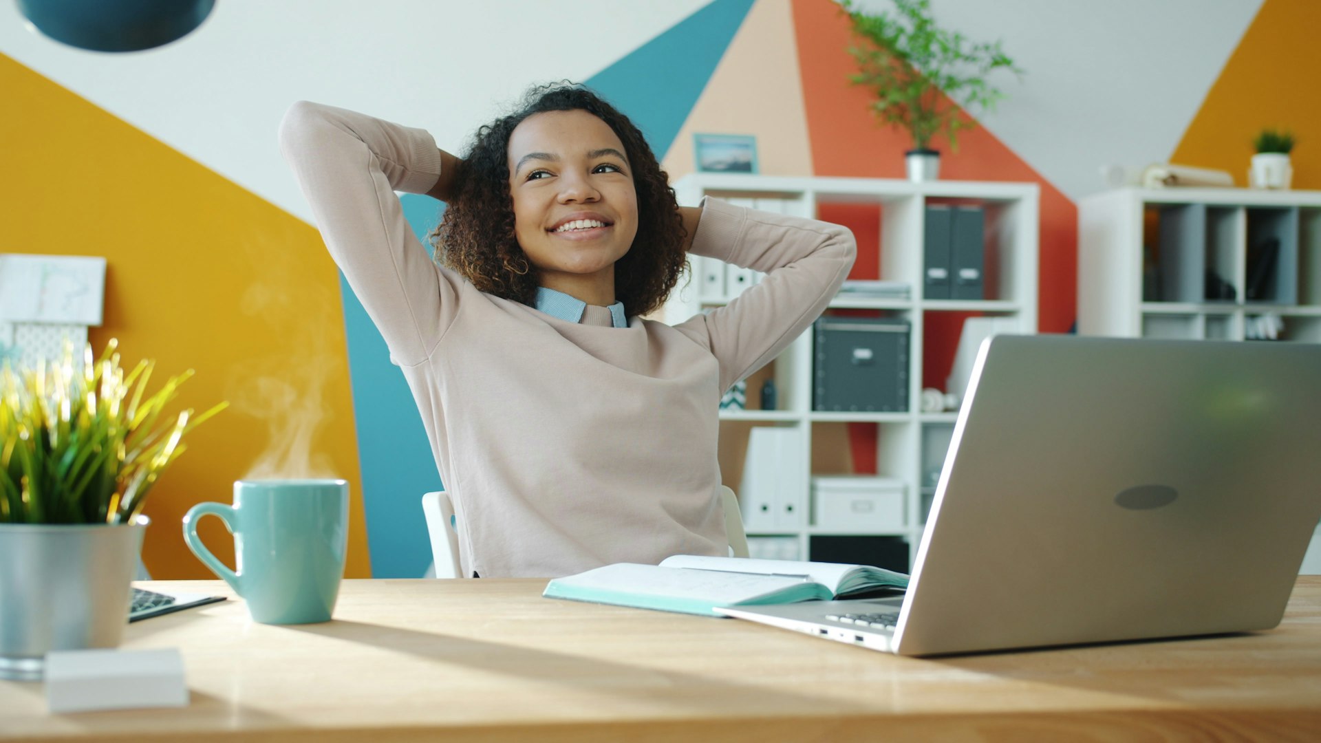 Woman relaxing at desk with laptop and coffee.